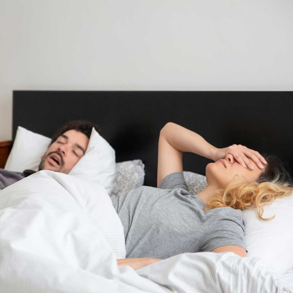 une femme se tient la tête car son mari ronfle et l'empeche de dormir